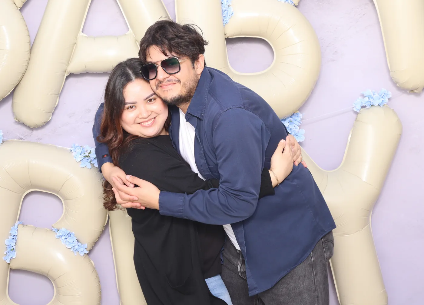 A couple hugging in front of giant balloon letters spelling baby